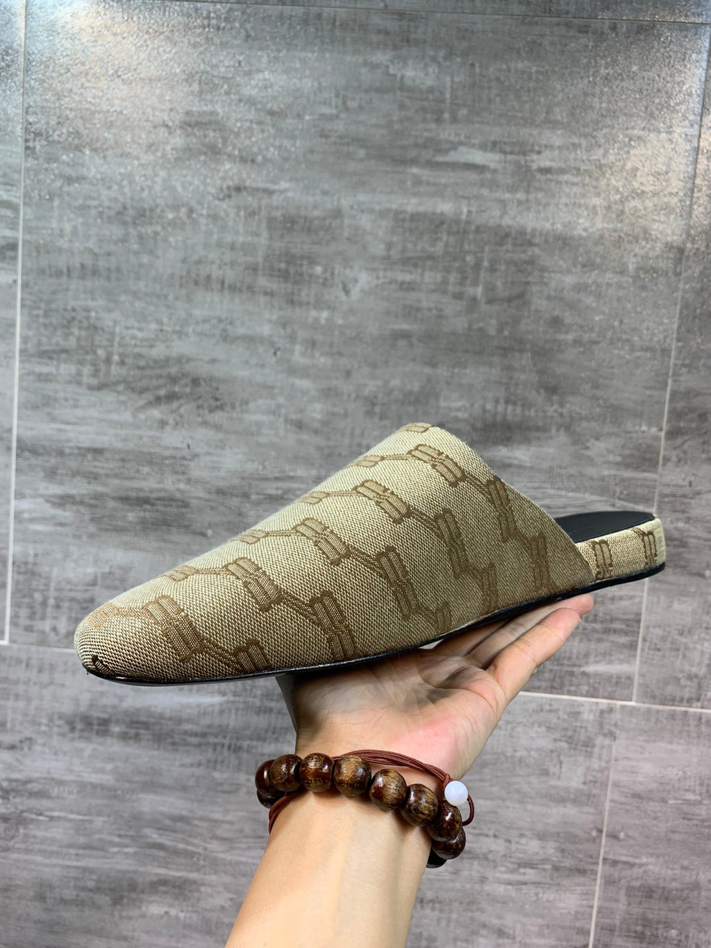 Beige patterned slide sandal held in hand, open side and black insole visible