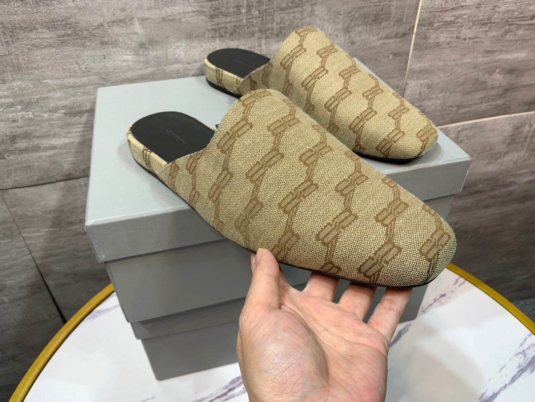 Beige patterned slide sandals held above a white display box, side view