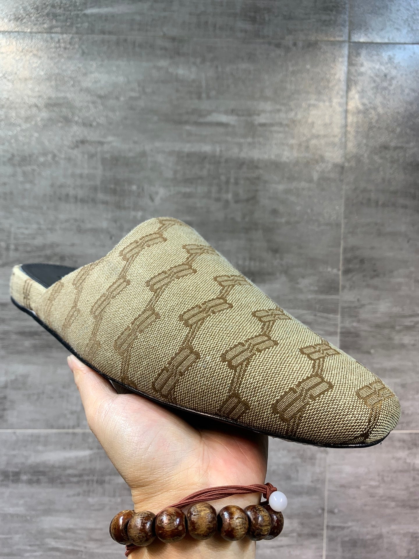 Beige patterned slide sandal held in hand, sole edge and black insole visible