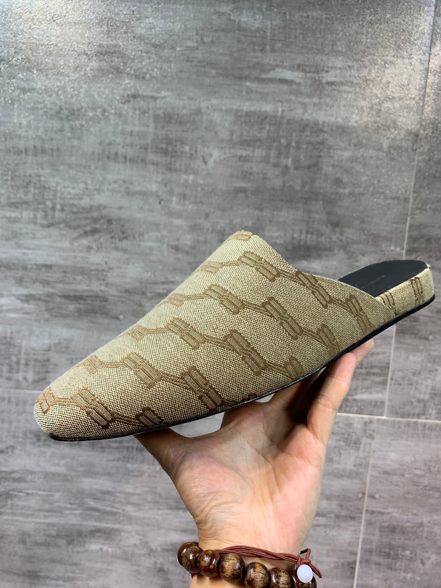 Beige patterned slide sandal held in hand, side profile and black insole