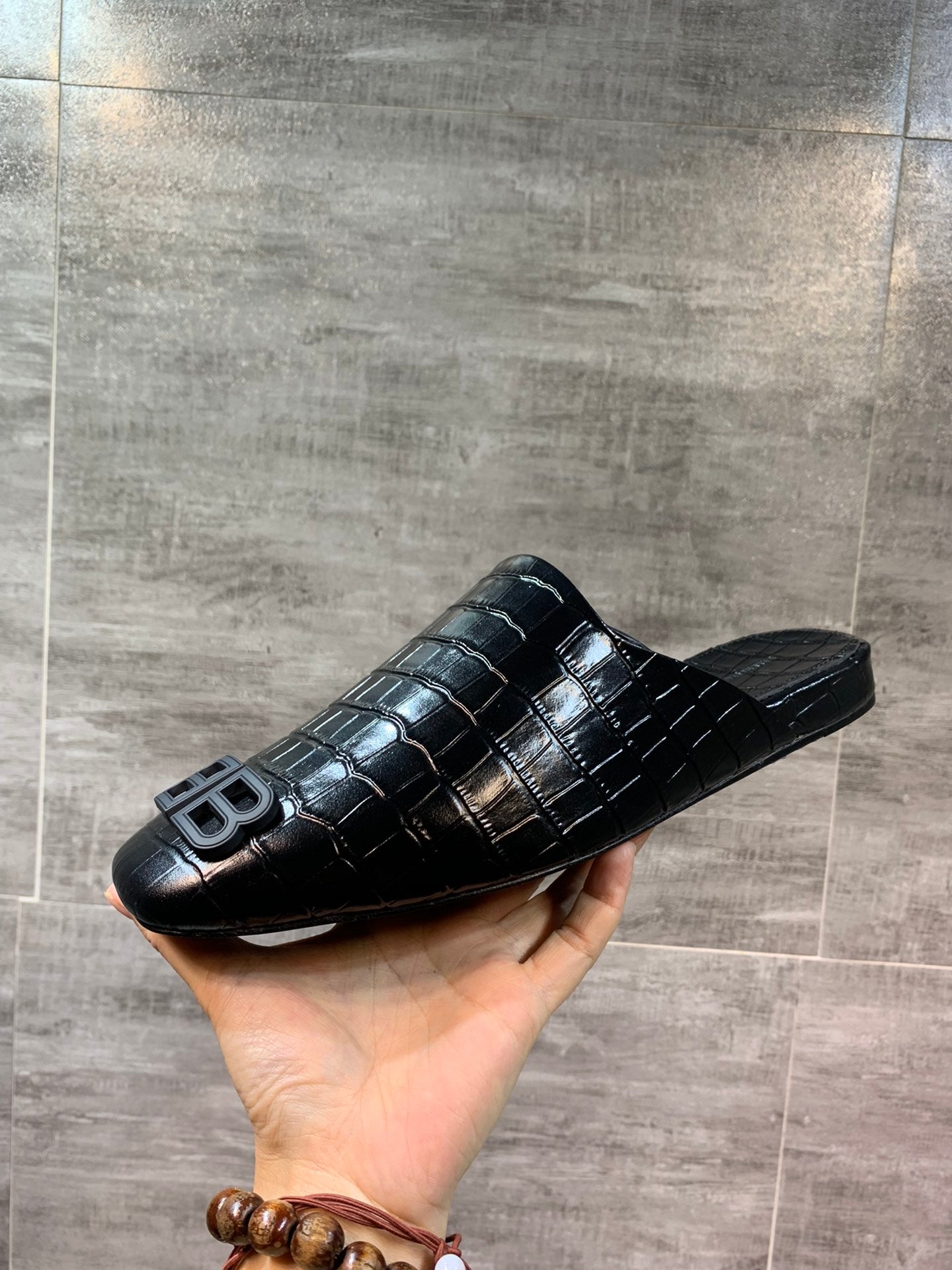 Black croc-embossed slide sandal with BB logo, angled in hand