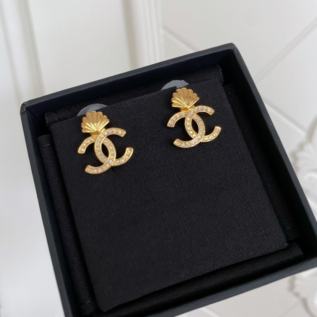 Chanel stud earrings with gold-tone CC shell design on dark fabric backing