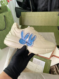 Cream Gucci lace-up sneakers with blue rabbit graphic on the side.