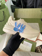 Cream Gucci lace-up sneakers with blue rabbit graphic on the side.