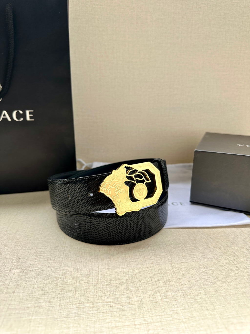 Black leather belt with textured strap and gold-tone crest buckle, laid on white cloth