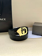 Black leather belt with textured strap and gold-tone crest buckle, laid on white cloth