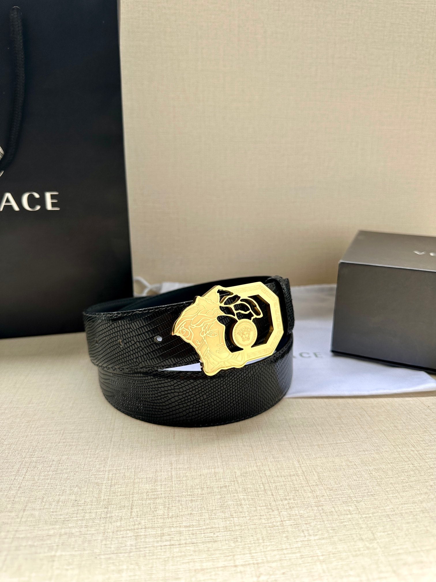 Black leather belt with textured strap and gold-tone crest buckle, laid on white cloth