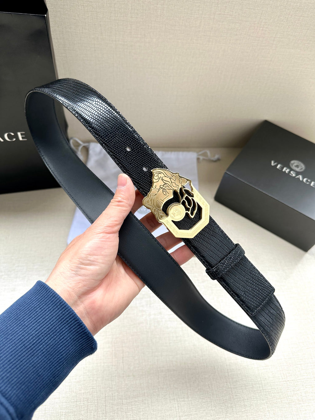 Black leather belt with textured strap and gold-tone crest buckle, held in hand