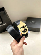 Black textured leather belt with gold-tone crest buckle, close-up held by hand