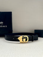 Black leather belt with textured strap and gold-tone crest buckle, flat on surface