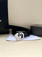 Black leather belt with wide strap and silver-tone crest buckle on display with box