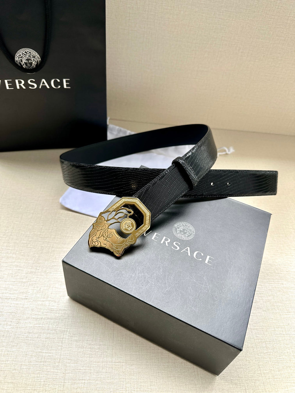 Black leather belt with textured strap and gold-tone crest buckle on box display