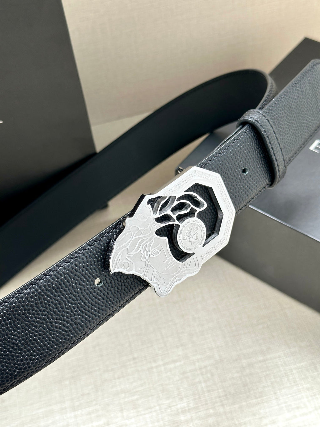 Versace leather belt, dark textured strap and large silver logo buckle close-up