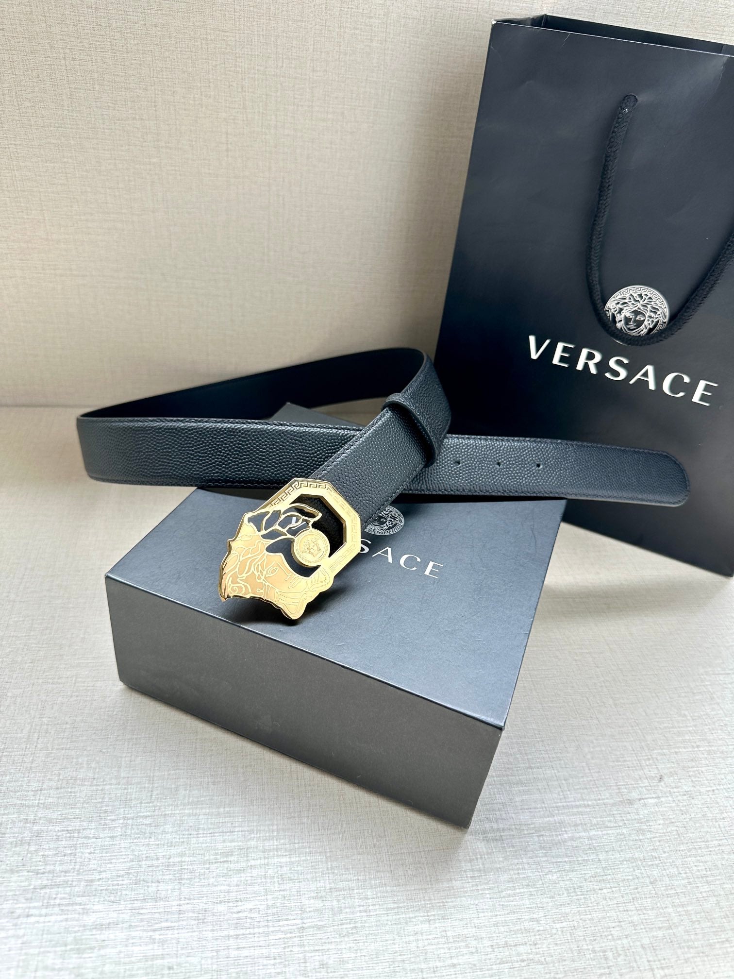 Versace leather belt, dark strap with gold logo buckle beside gift box