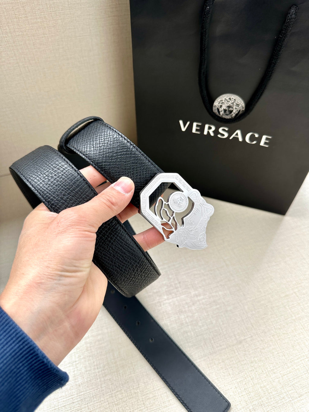 Black textured leather belt with silver-tone Medusa logo buckle and belt holes.