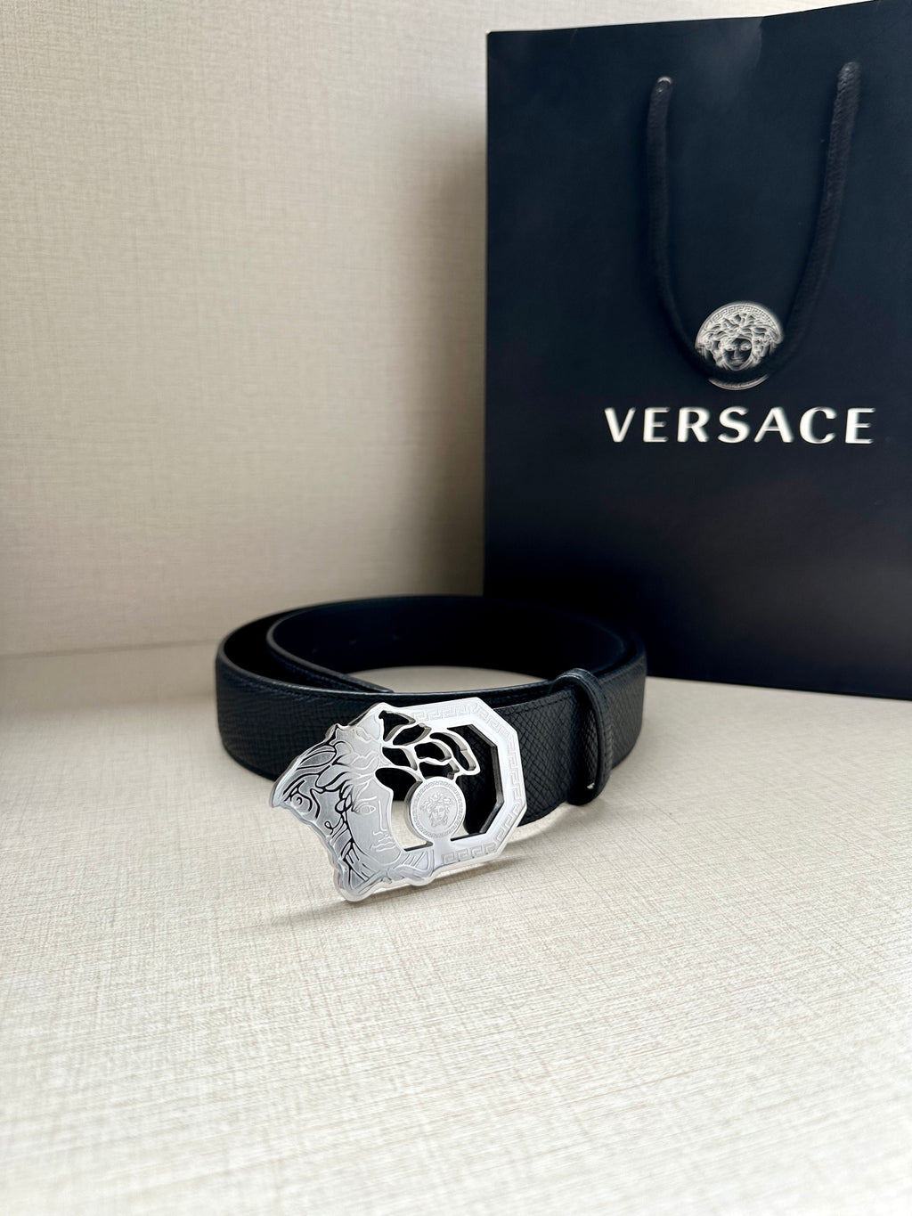 Black leather belt with silver-tone Medusa buckle and textured strap.