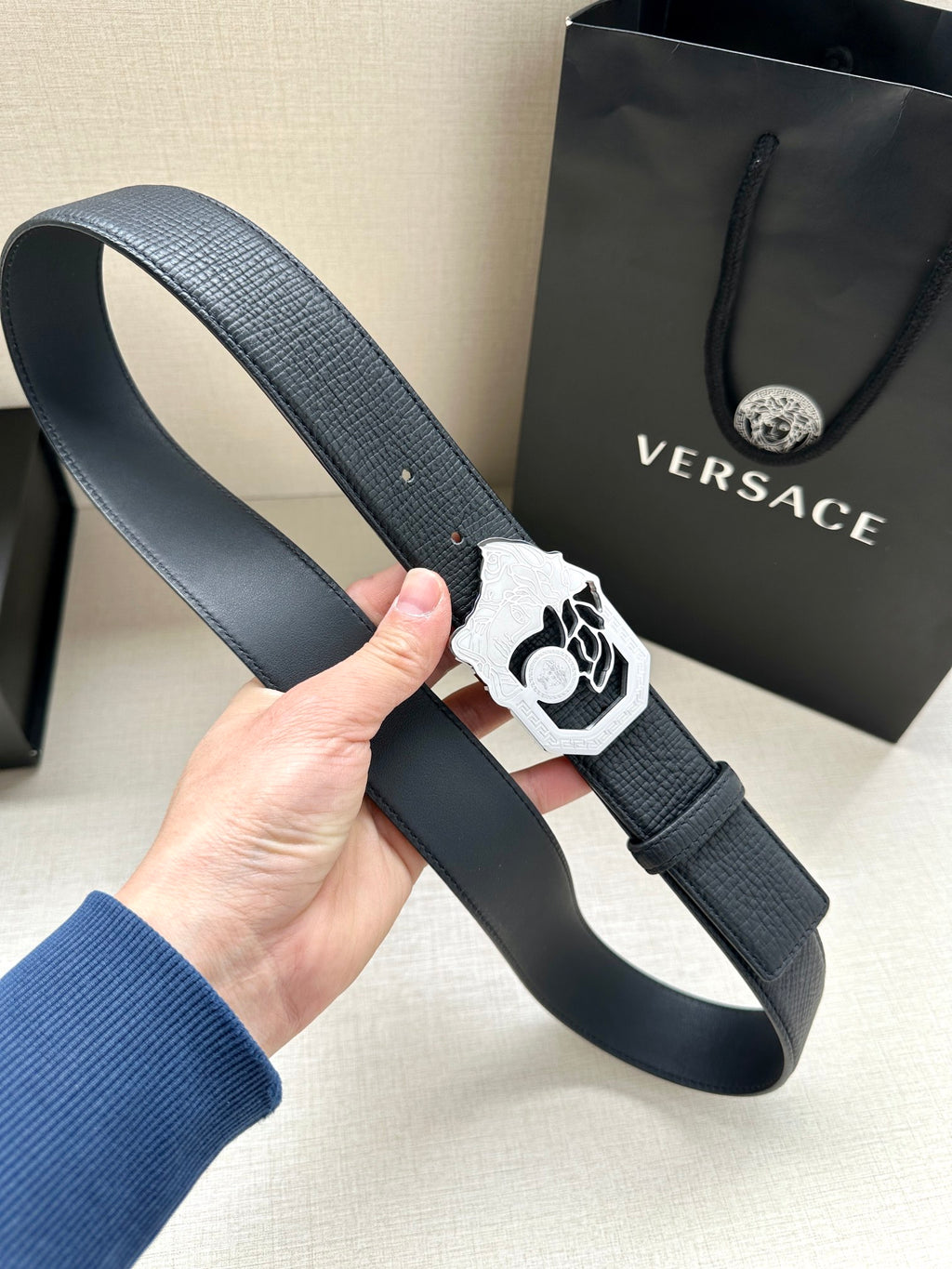 Dark navy leather belt with white/silver Medusa buckle and metal pin holes.