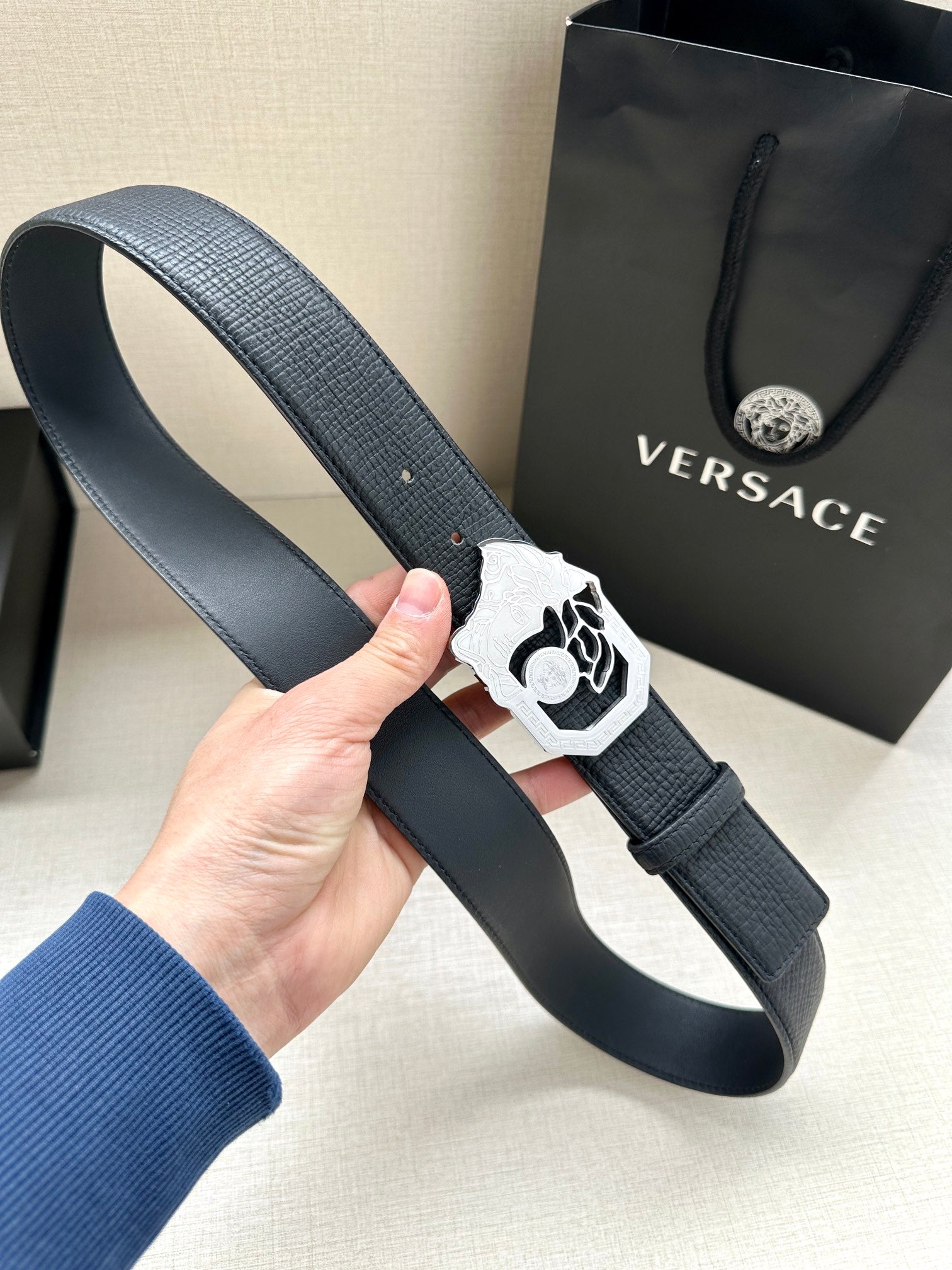 Dark navy leather belt with white/silver Medusa buckle and metal pin holes.