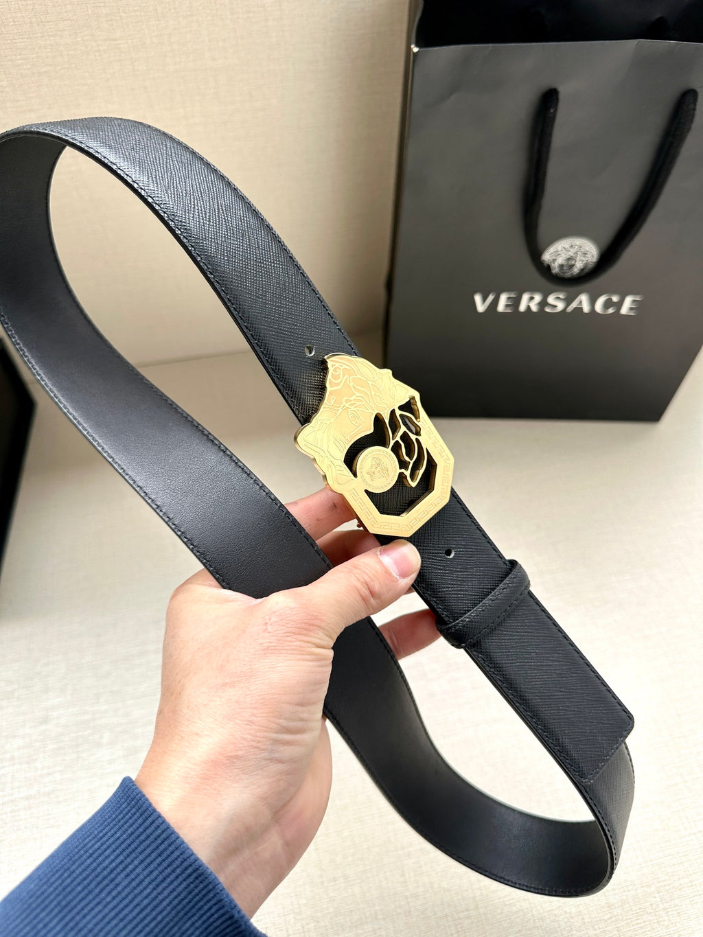 Dark blue leather belt with gold Medusa emblem buckle and stitched edge.