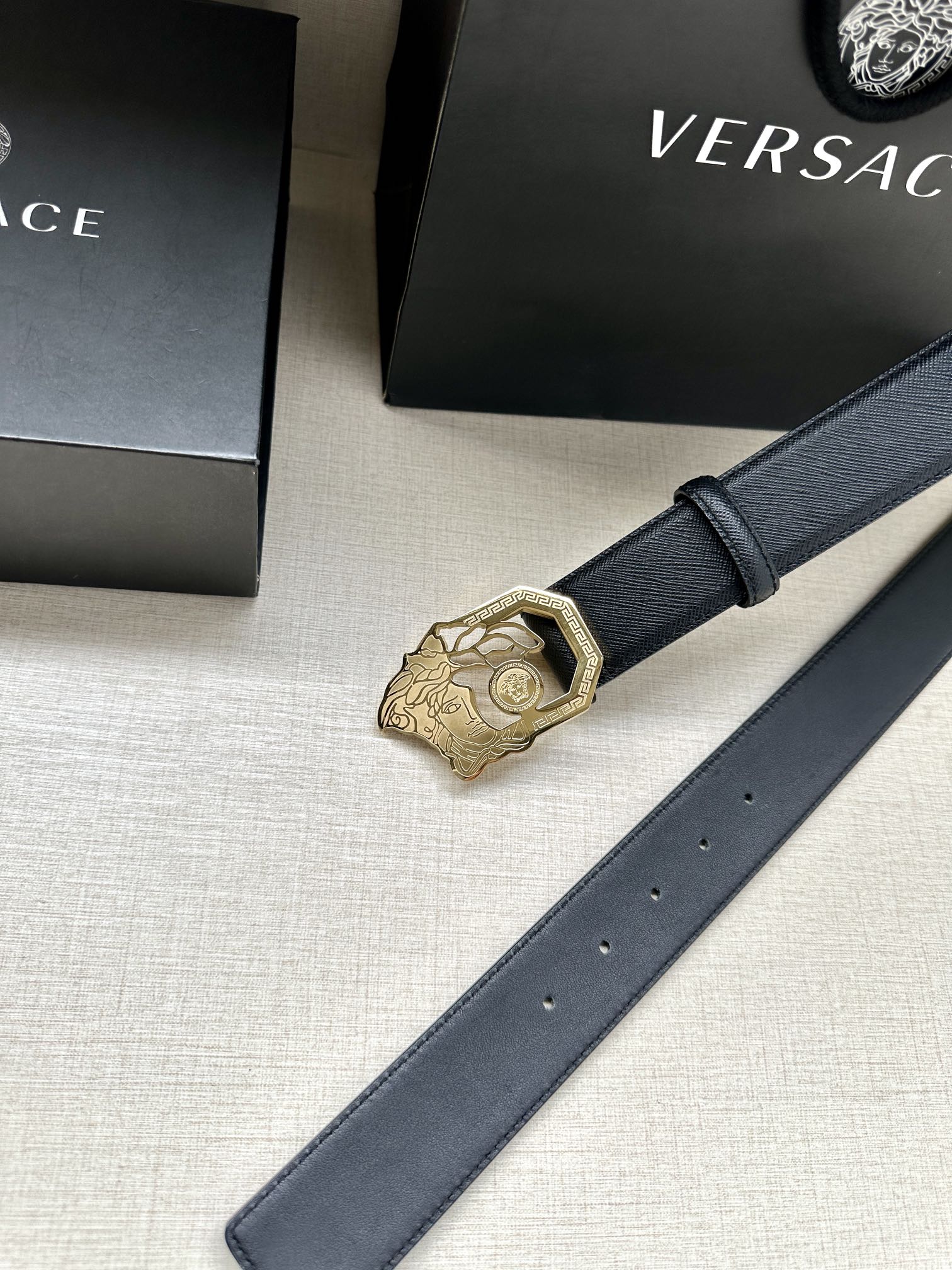 Dark blue leather belt with gold Medusa emblem buckle and eyelet holes.