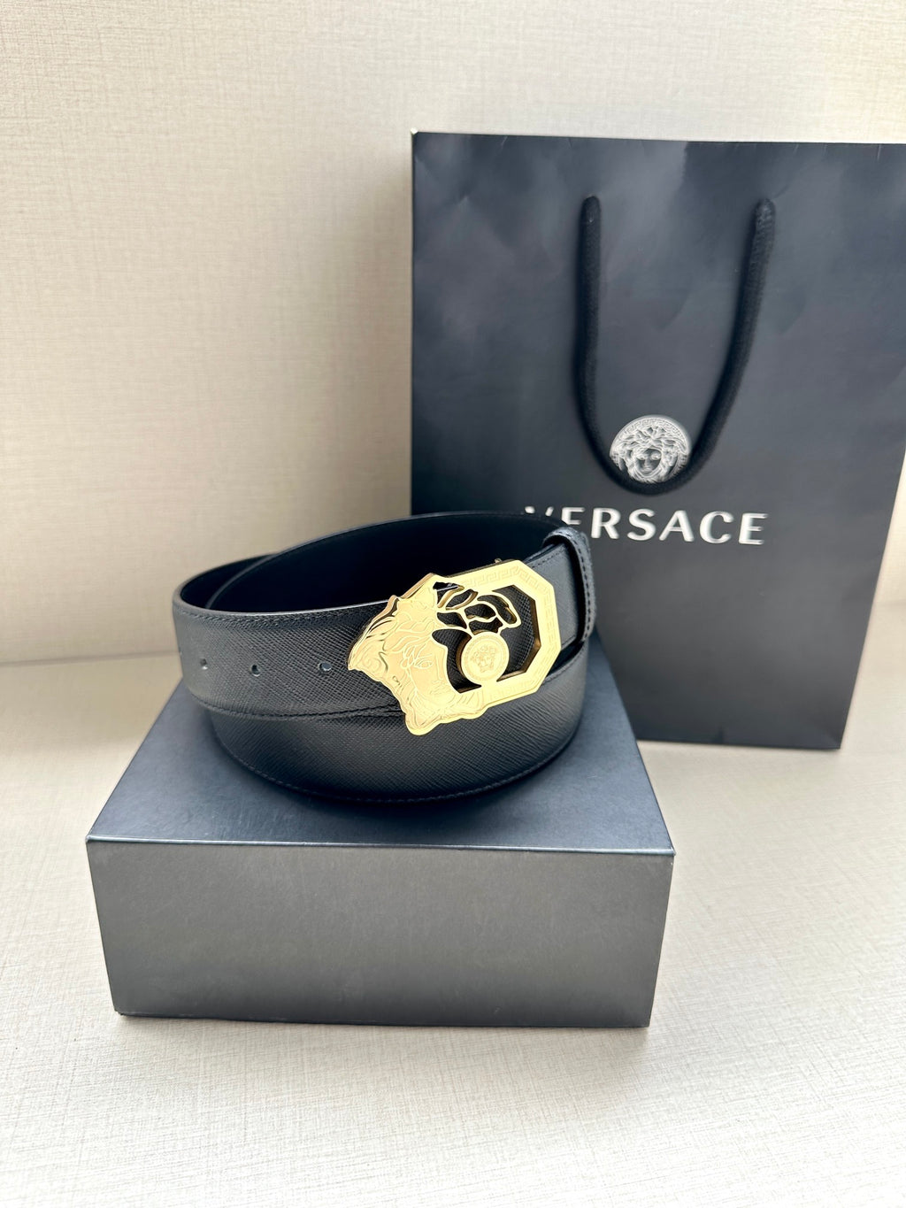 Dark blue leather belt with gold Medusa emblem buckle, front view.