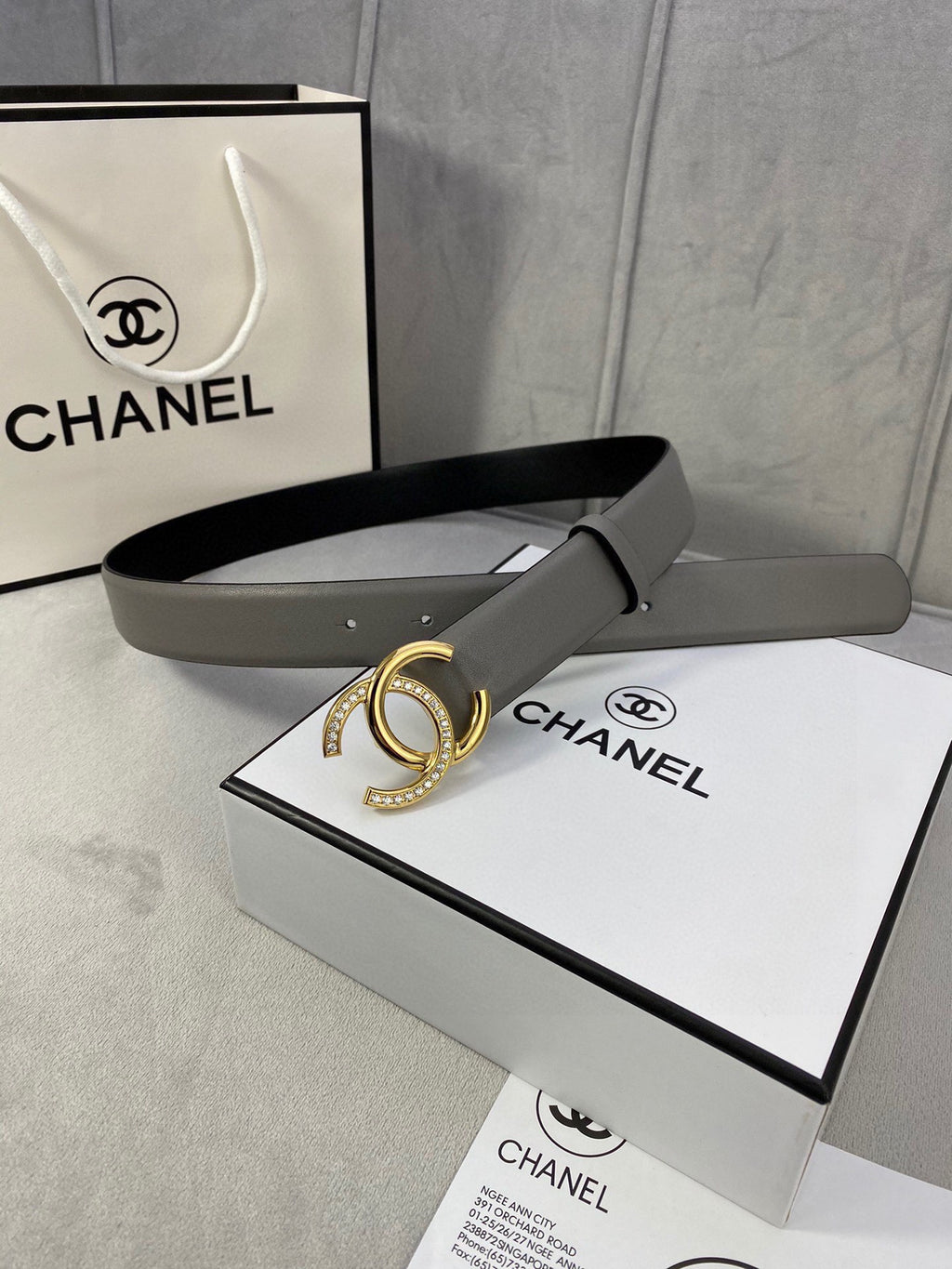 Leather belt with gray strap and gold-tone double C buckle, shown with packaging box