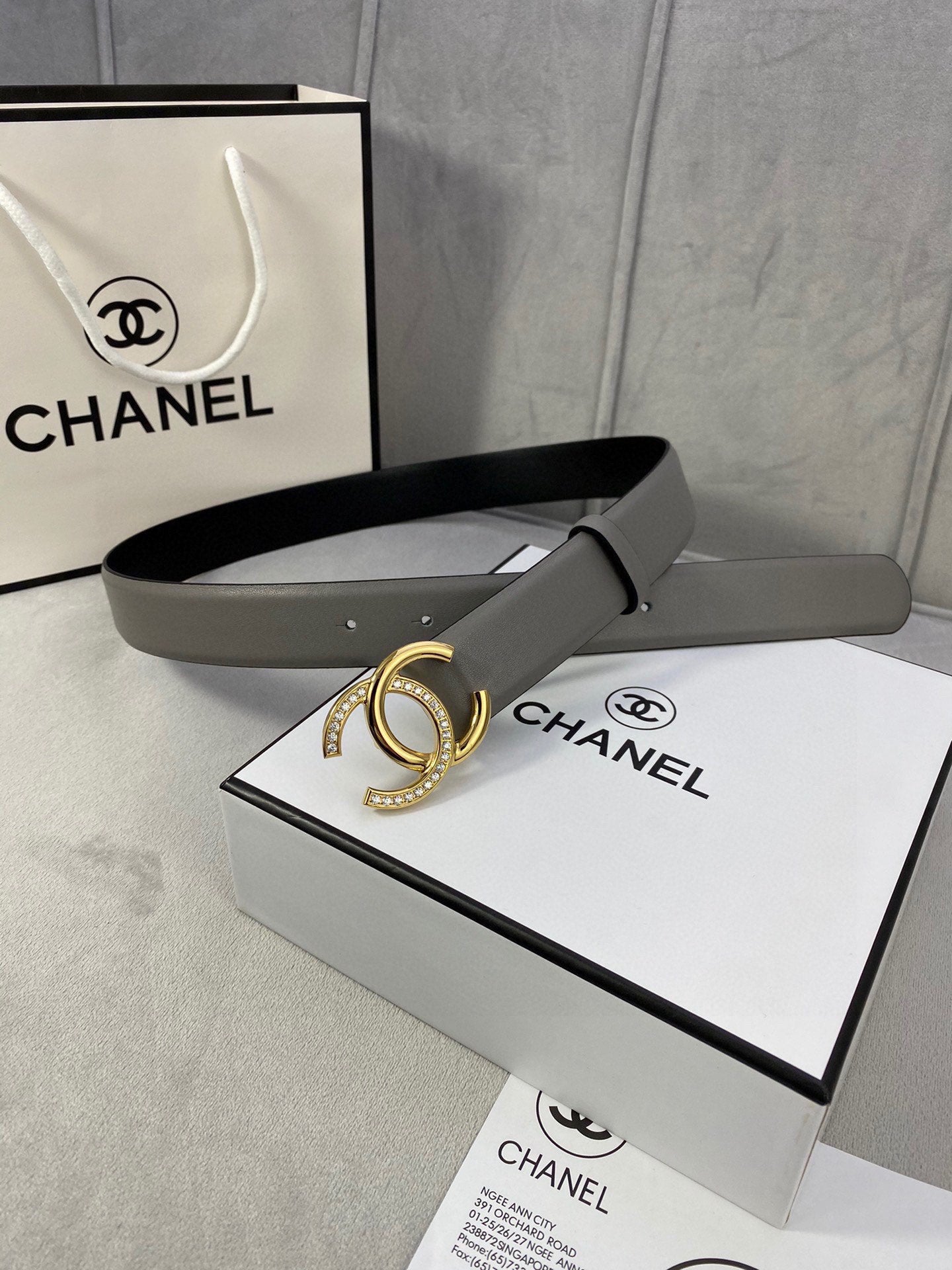 Leather belt with gray strap and gold-tone double C buckle, shown with packaging box