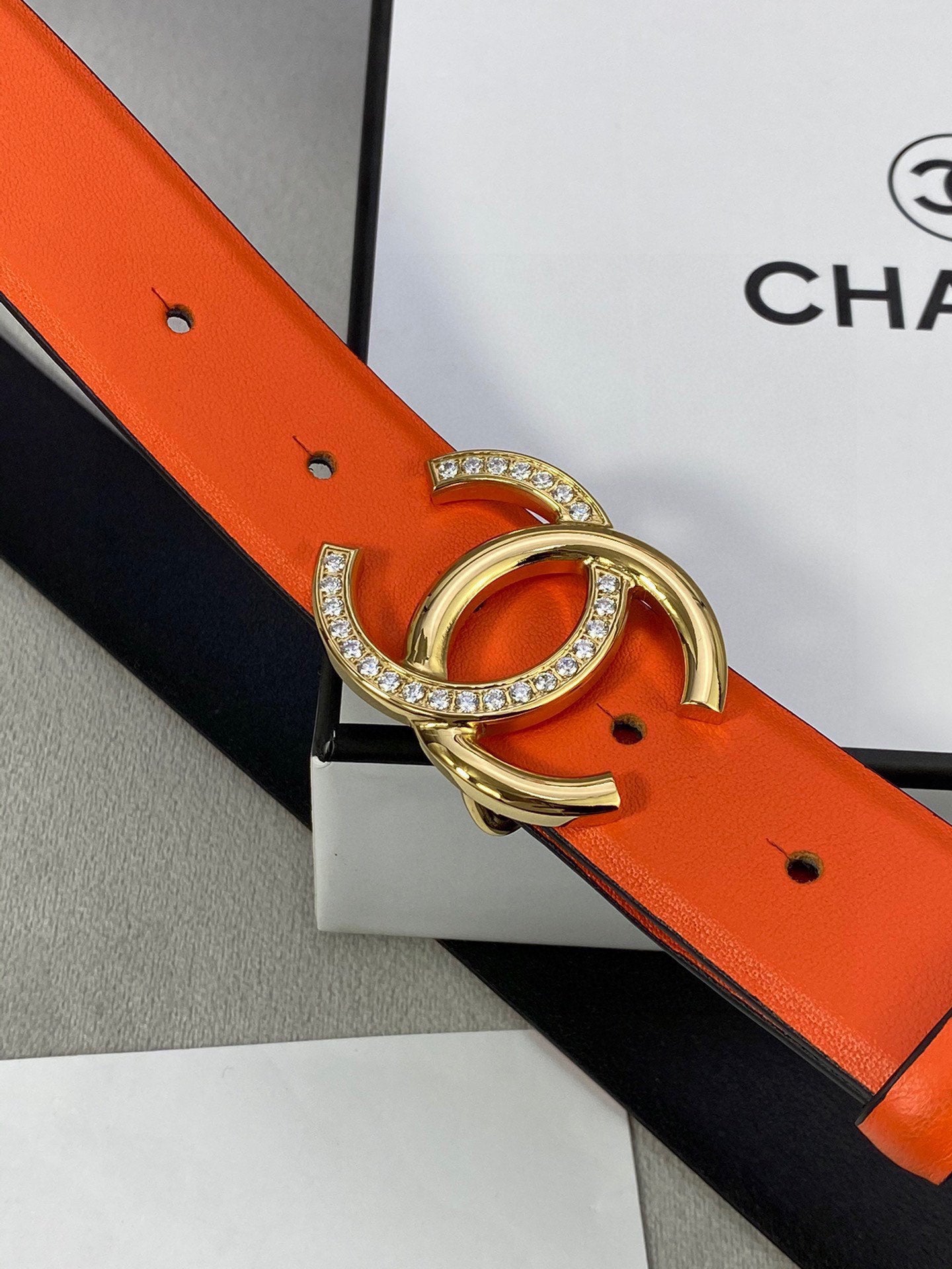 Close-up: orange leather belt with gold-tone CC buckle and rhinestone trim