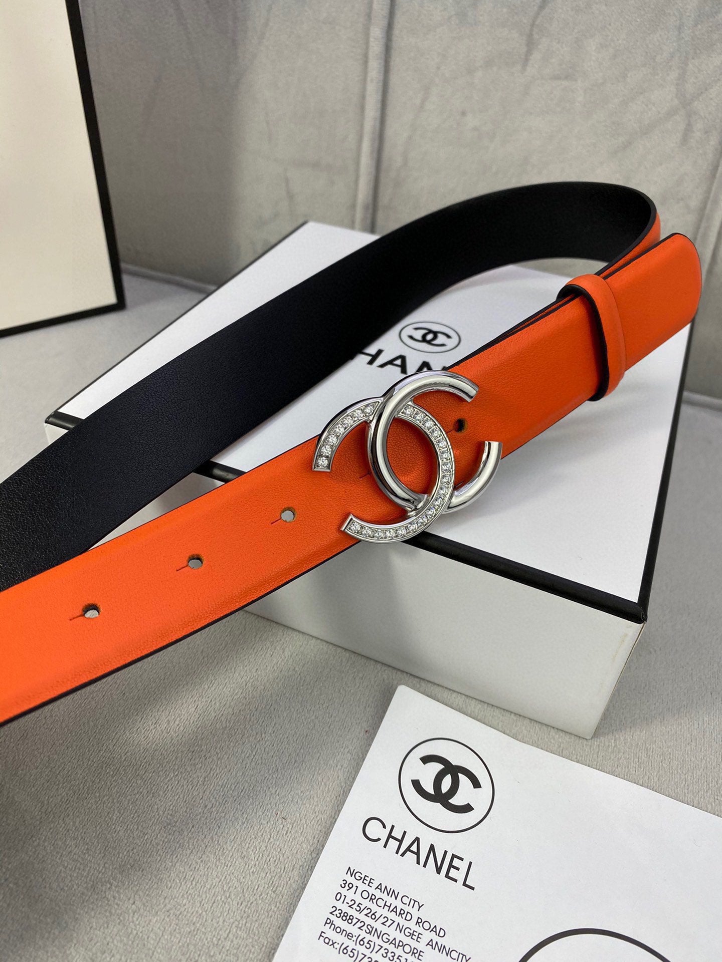 Orange leather belt with silver CC buckle and black fabric backing