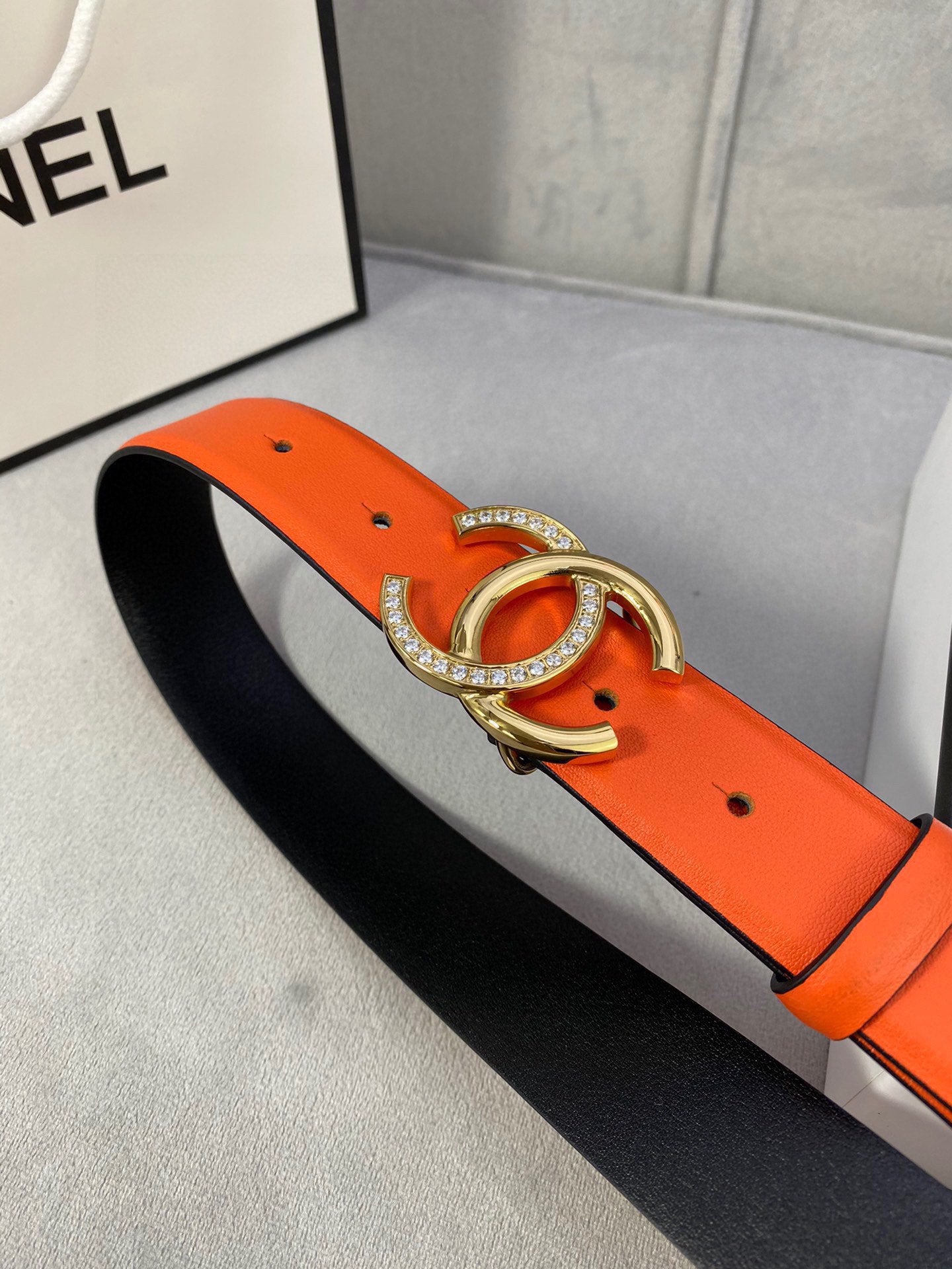 Orange leather belt with gold-tone CC buckle and rhinestone accents