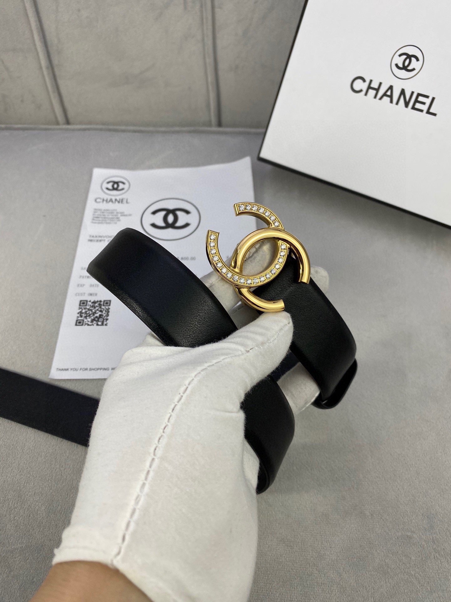Black leather belt with gold-tone CC buckle held in white glove