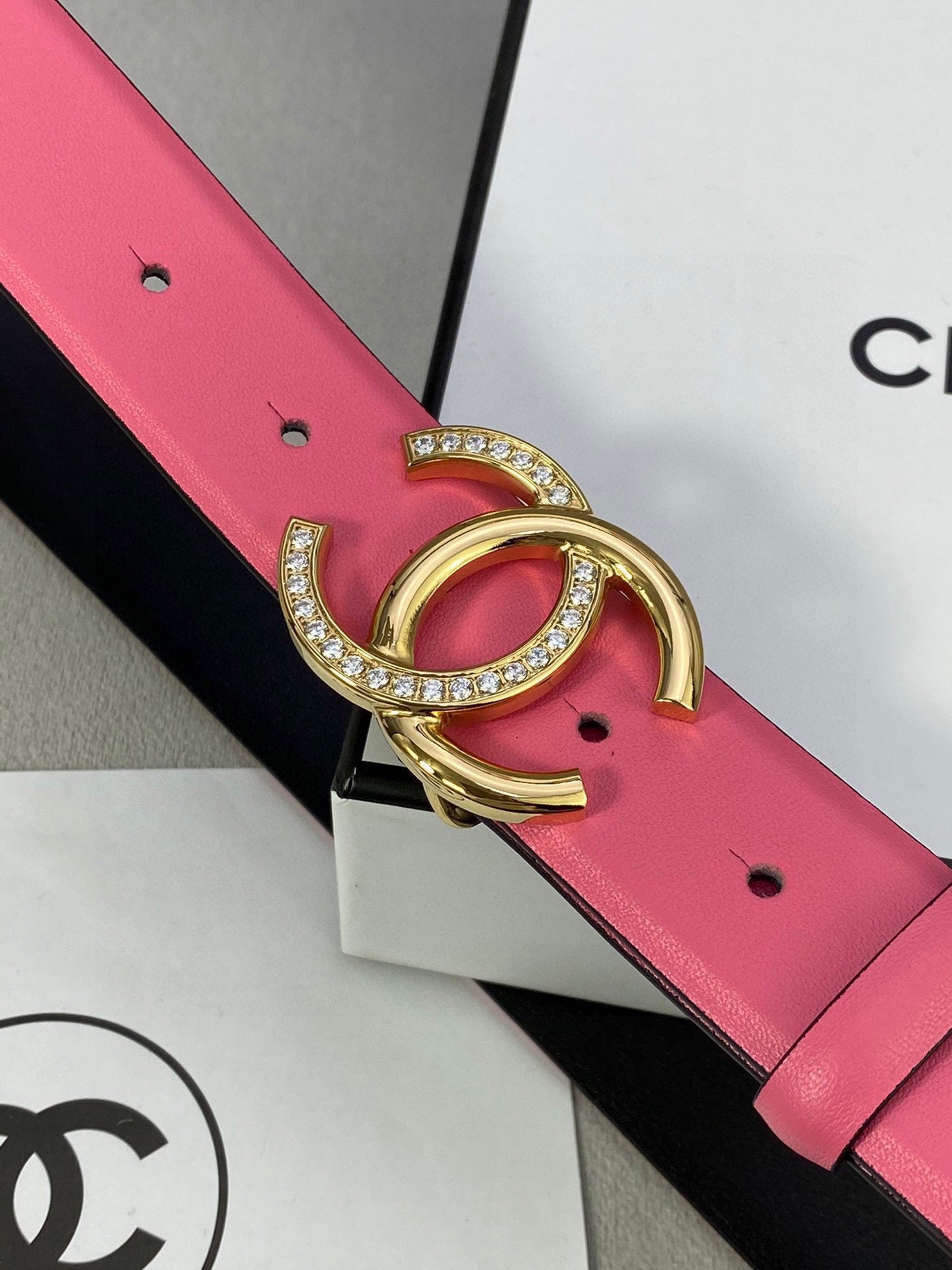 Chanel belt close-up: pink leather strap with gold rhinestone CC buckle on black backing