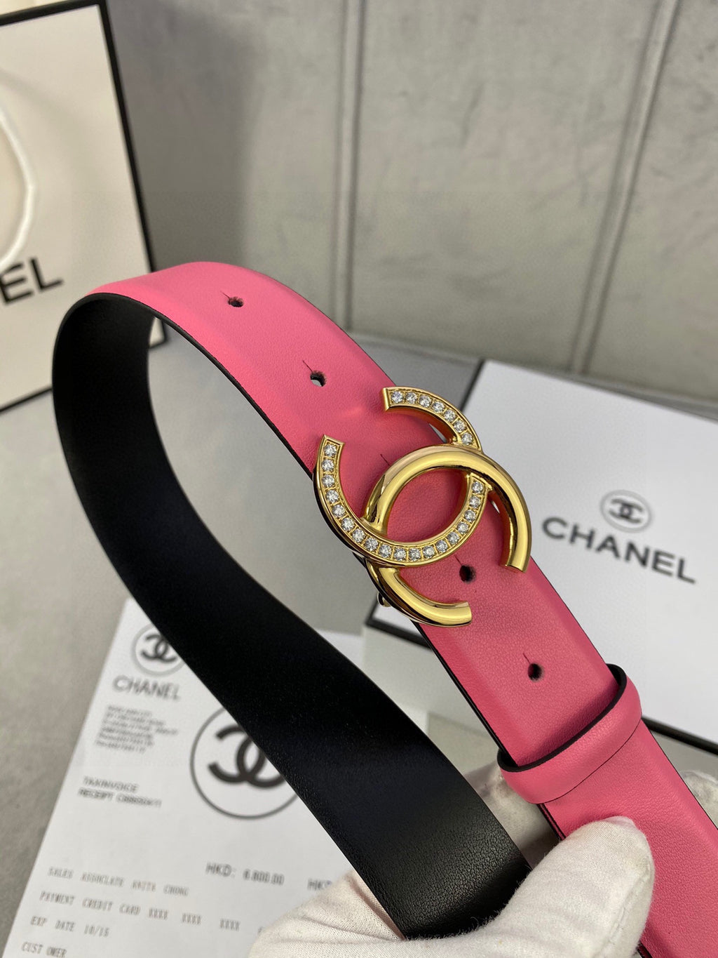 Chanel belt close-up: pink strap with black underside and gold rhinestone CC buckle