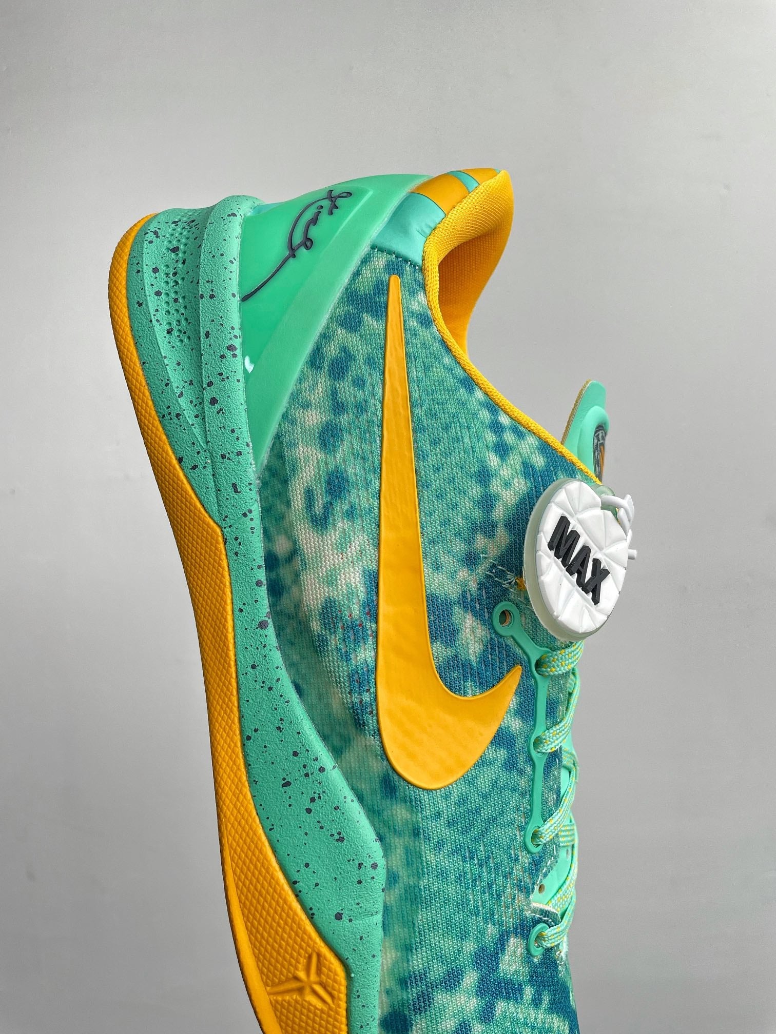 Teal basketball shoe with yellow swoosh stripe and lace eyelets, side view