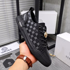 Black low-top sneakers in hand; patterned side panels, lace-up, gold emblem detail