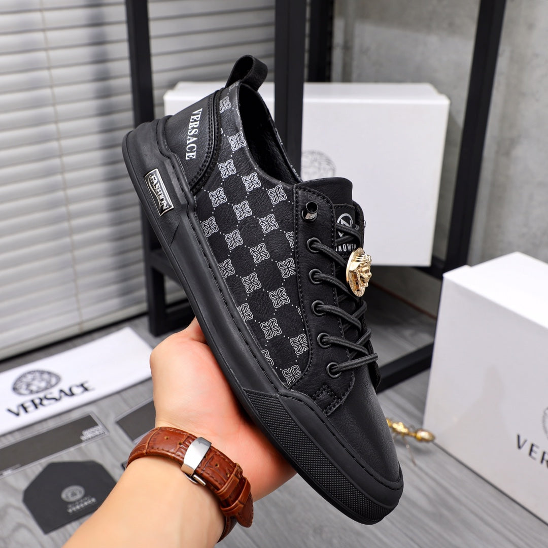 Black low-top sneakers in hand; patterned side panels, lace-up, gold emblem detail