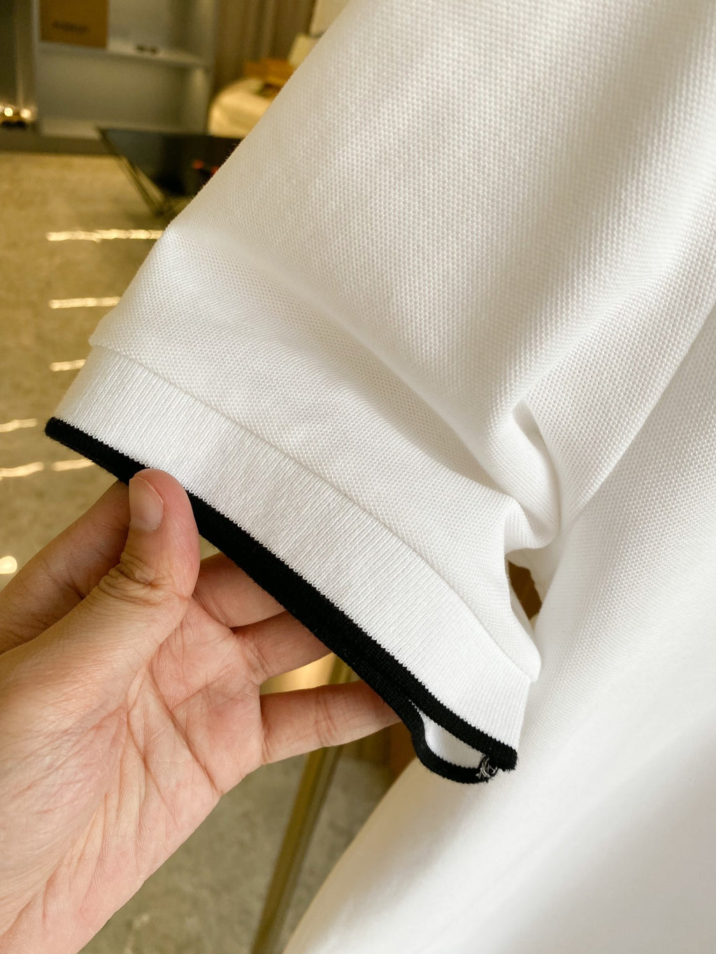 Sleeve hem detail of white polo shirt with black-trim edge