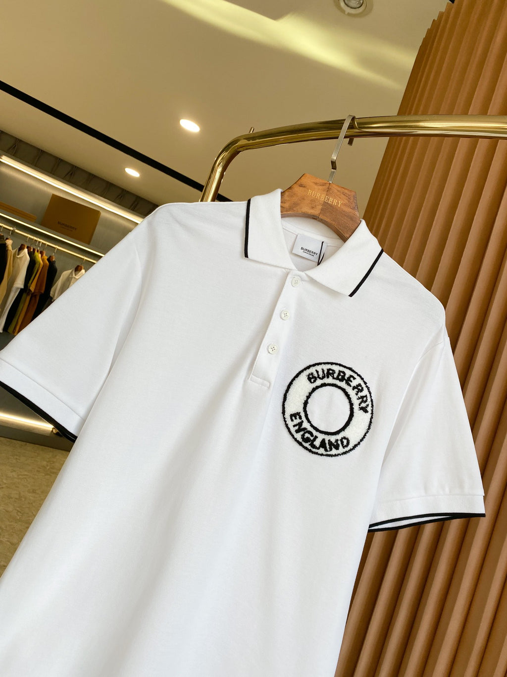 White polo shirt on hanger, black-trim collar with Burberry England logo at chest