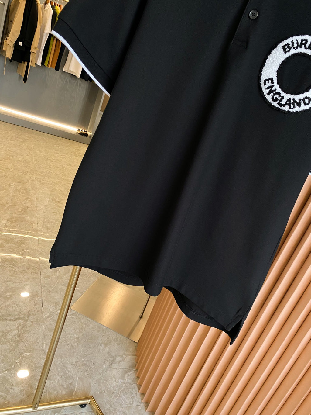 Black polo shirt side view with short sleeves and curved hem, white-trimmed sleeve edge