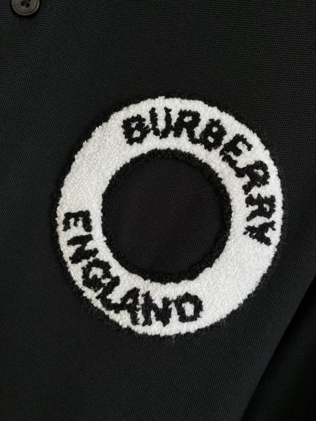 Circular logo patch on black polo shirt with white embroidered text
