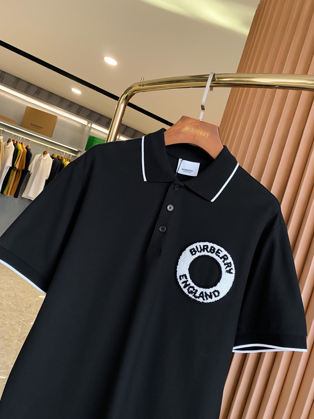 Black polo shirt front with short sleeves, white-trimmed collar, button placket, circular logo