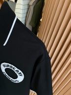 Black polo shirt shoulder detail with circular logo patch and white-trimmed sleeve edge