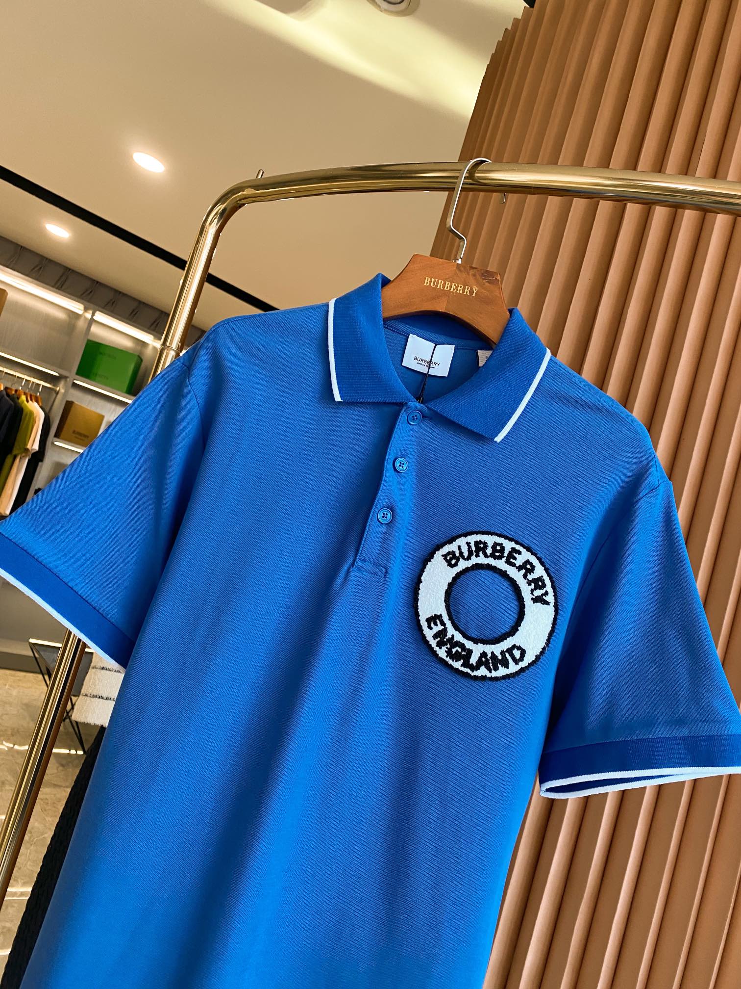 Blue polo shirt on a hanger with white-trim collar and Burberry England logo patch