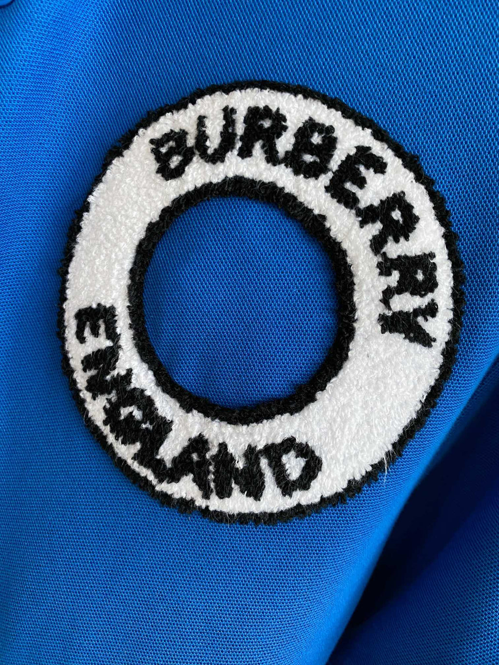 Close-up of Burberry England round logo patch on a blue polo shirt