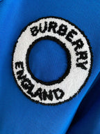 Close-up of Burberry England round logo patch on a blue polo shirt