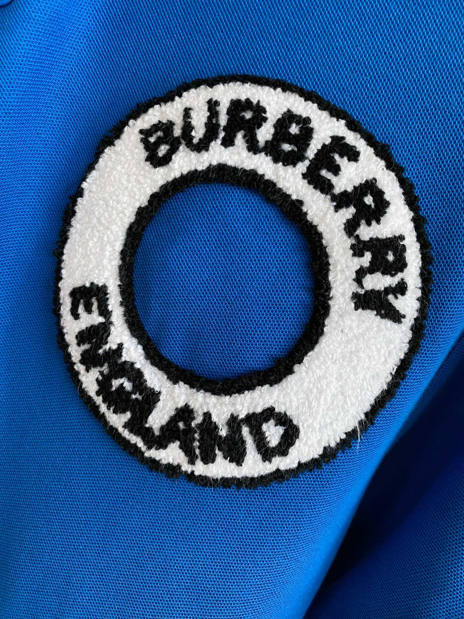 Close-up of Burberry England round logo patch on a blue polo shirt
