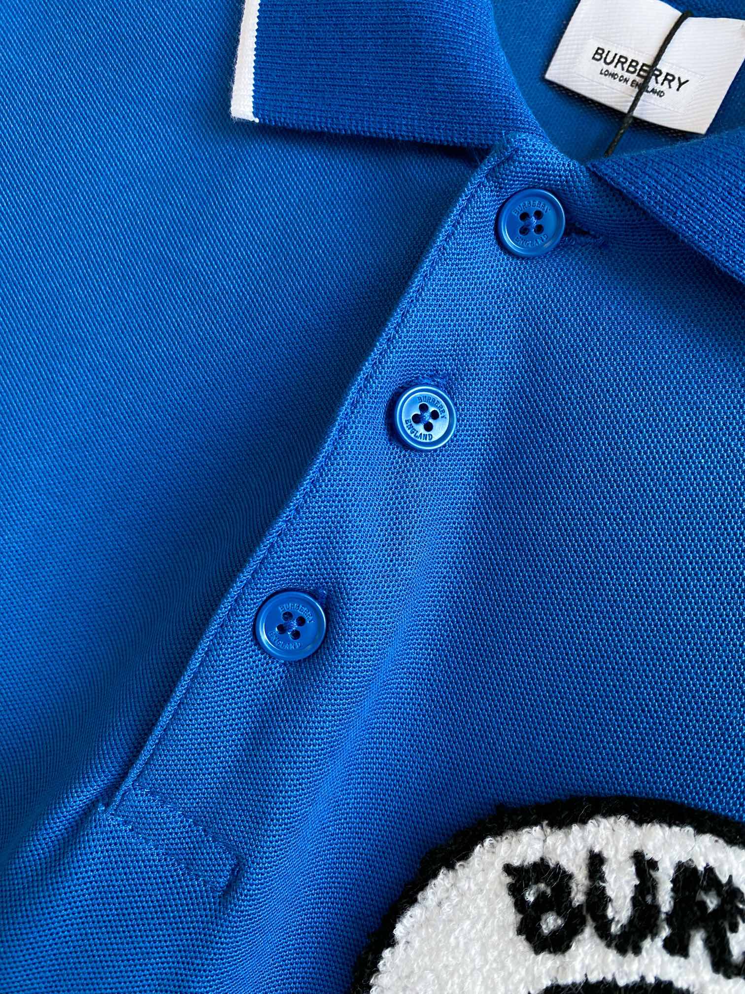 Blue polo shirt showing three button placket with blue buttons and white edge trim
