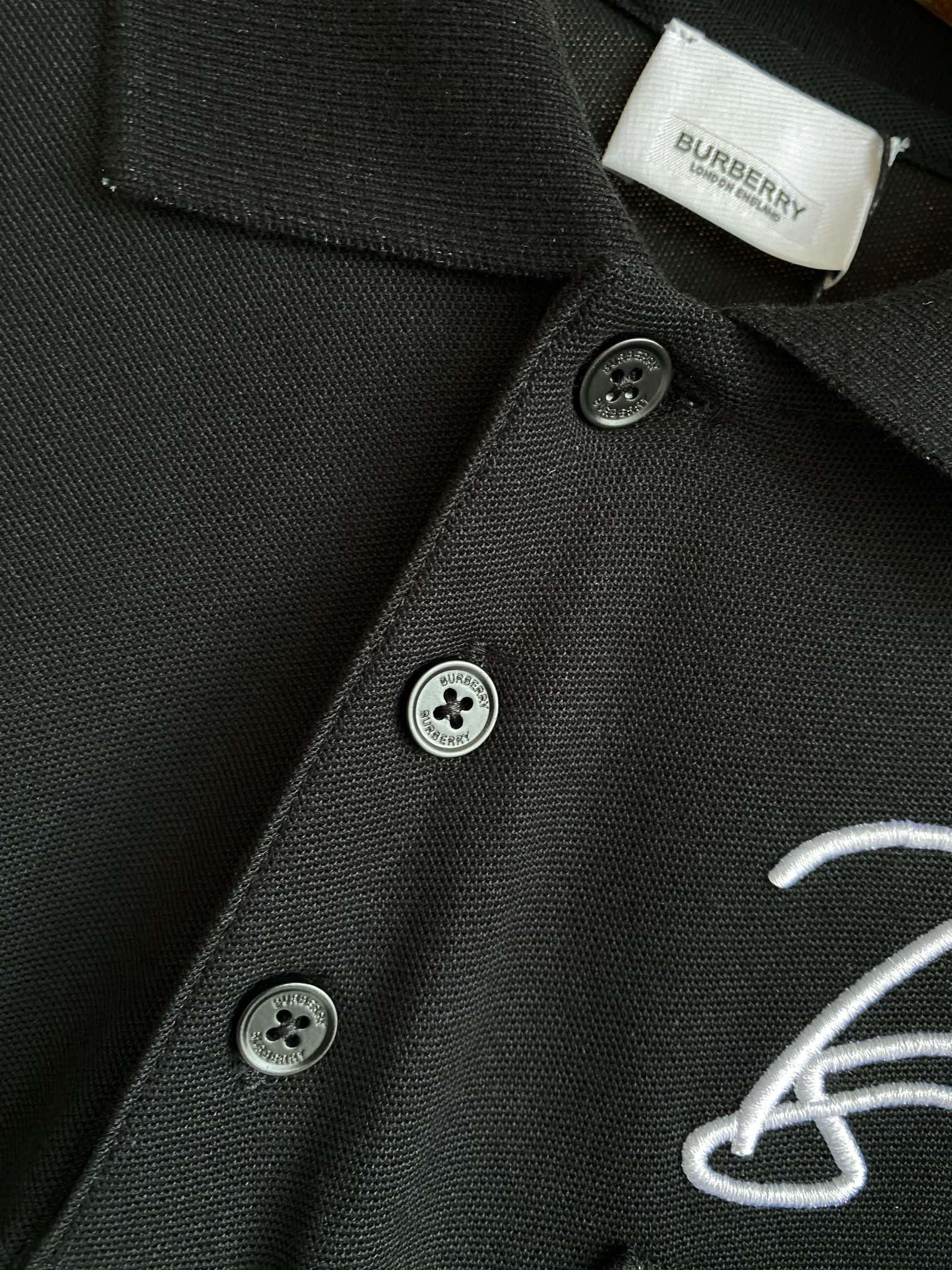 Black polo shirt collar and button placket with Burberry logo embroidery