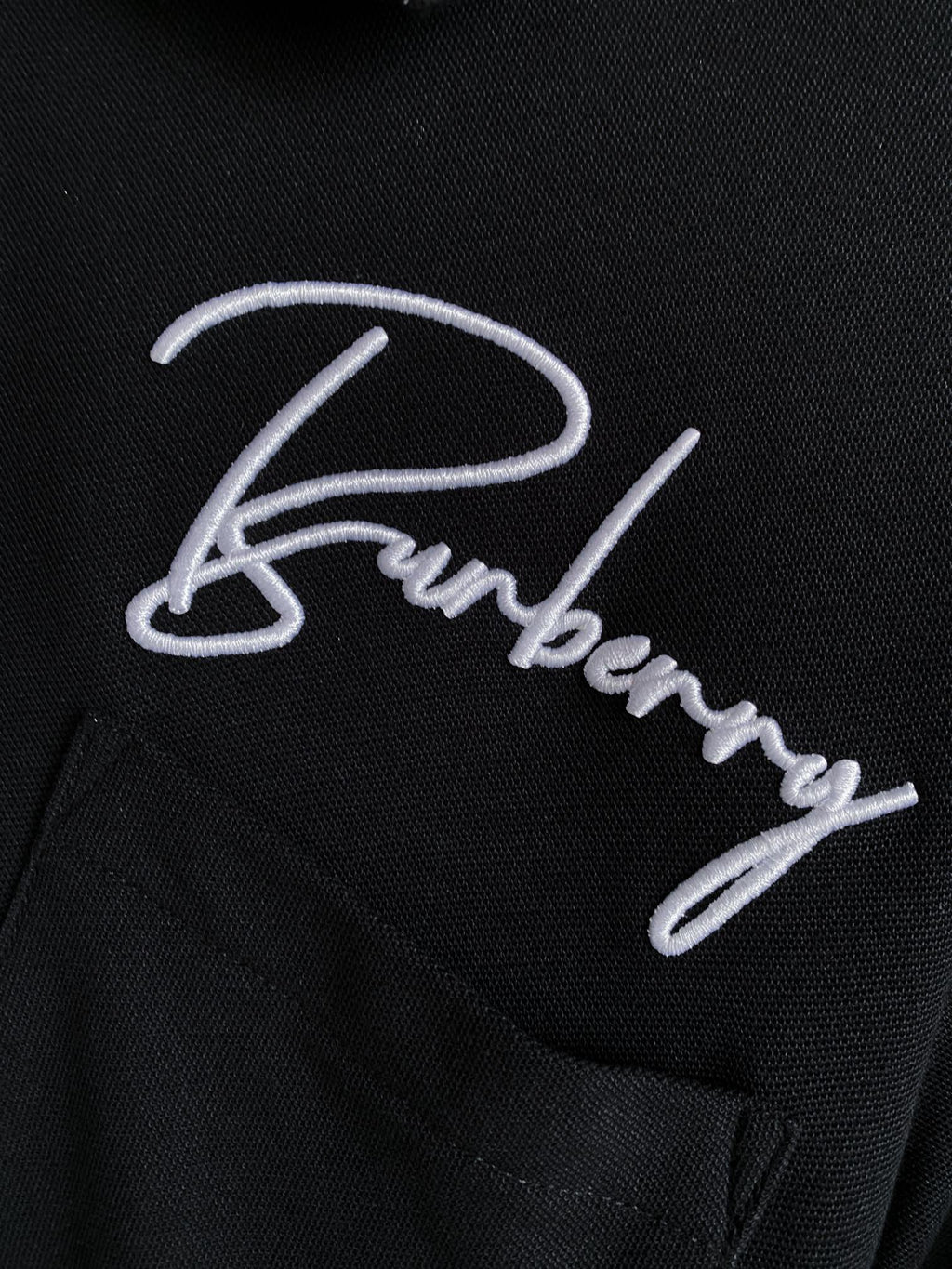 Close-up of black polo shirt with white Burberry logo embroidery and buttons