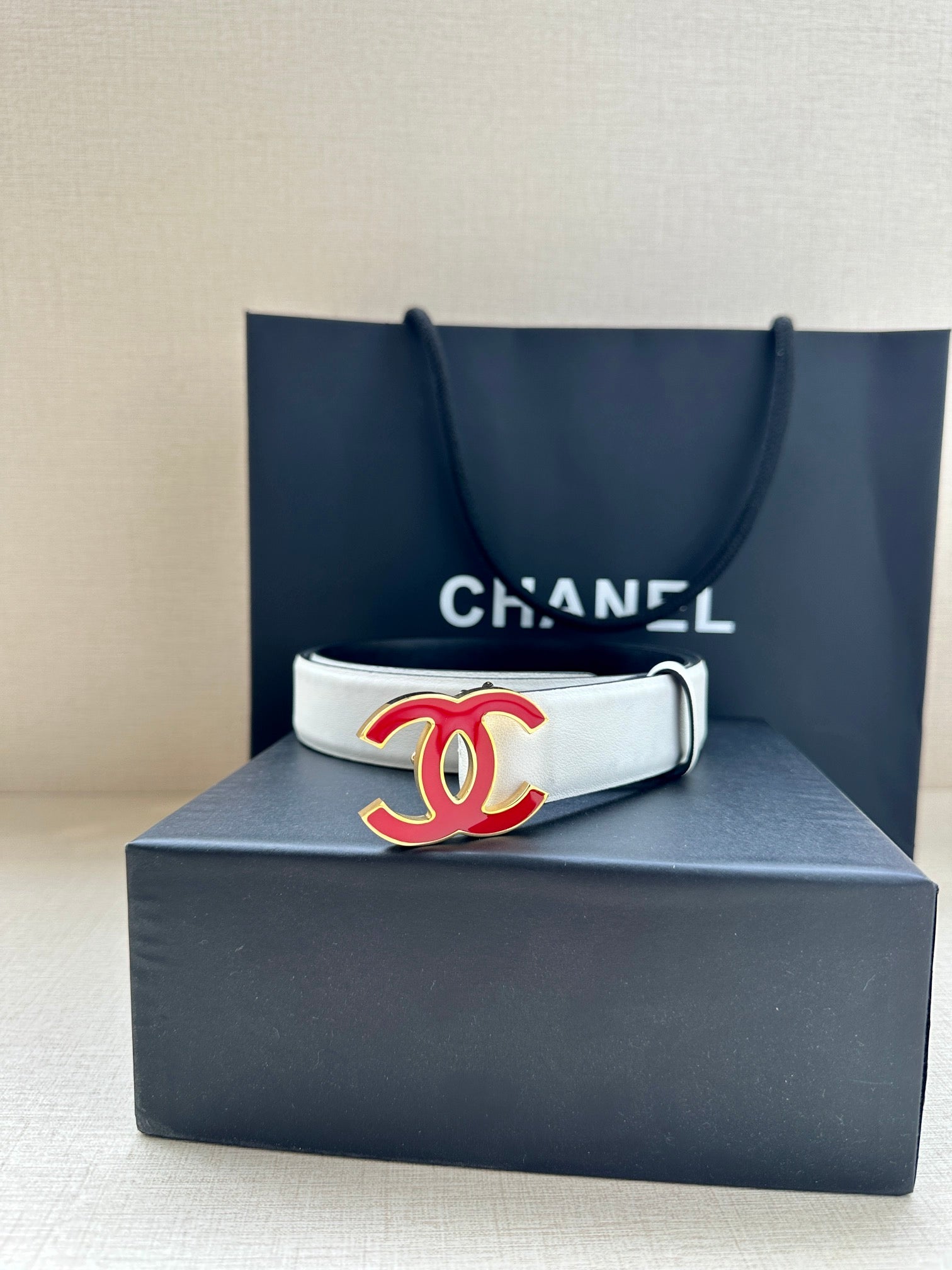 Leather belt with Chanel logo buckle on box, light cream strap with silver-tone holes